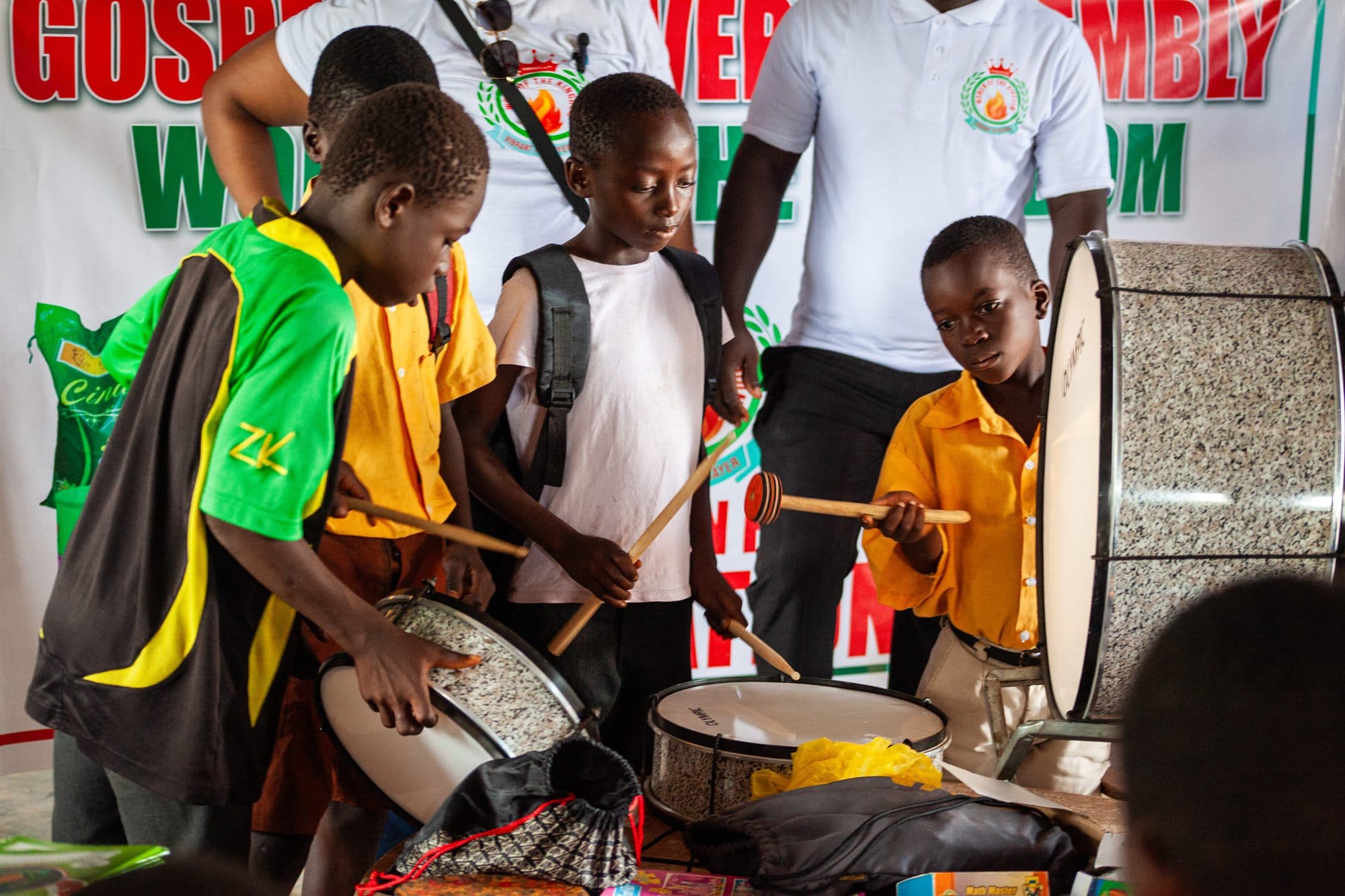 Boys playing donated drums in front of a Women of the Kingdom banner