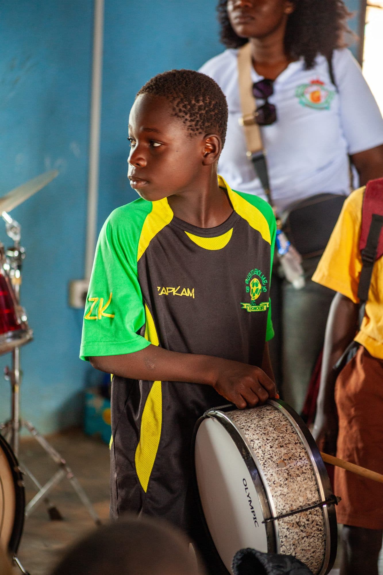 A boy in a green jersey playing a donated drum